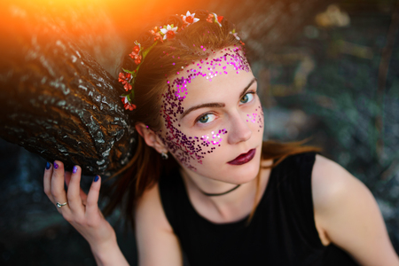 A young beautiful woman with a violet shine on her face stands near a burnt tree.の写真素材