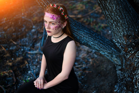 A young beautiful woman with a violet shine on her face stands near a burnt tree.