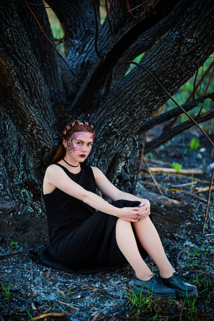 A young beautiful woman with a violet shine on her face stands near a burnt tree.の写真素材