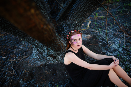 A young beautiful woman with a violet shine on her face stands near a burnt tree.の写真素材