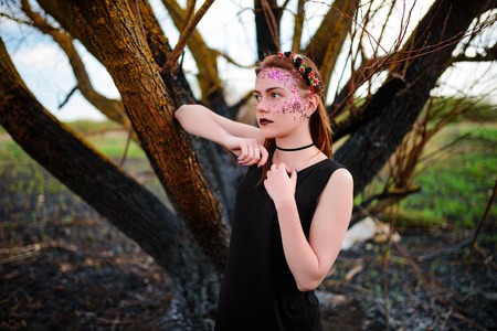 A young beautiful woman with a violet shine on her face stands near a burnt tree.の写真素材