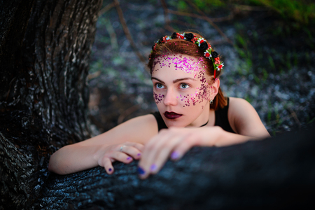 A young beautiful woman with a violet shine on her face sits near a burnt tree.の写真素材