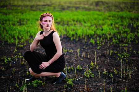 A young beautiful woman with a violet shine on her face stands near a burnt tree.の写真素材