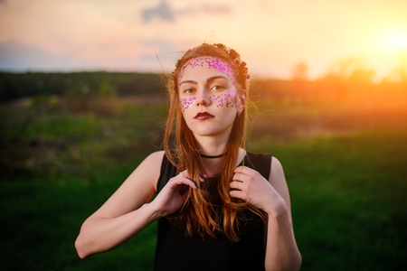 A young beautiful woman with a violet shine on her face standing on the grass and looking at the camera.の写真素材