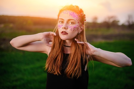 A young beautiful woman with a violet shine on her face standing on the grass and looking at the camera.の写真素材