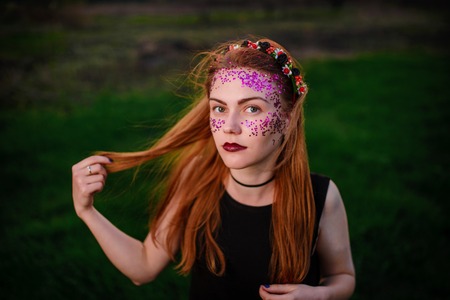 A young beautiful woman with a violet shine on her face standing on the grass and looking at the camera.の写真素材
