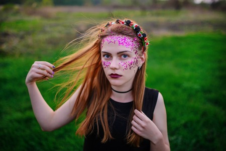 A young beautiful woman with a violet shine on her face standing on the grass and looking at the camera.の写真素材