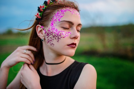 A young beautiful woman with a violet shine on her face standing on the grass and looking right.の写真素材