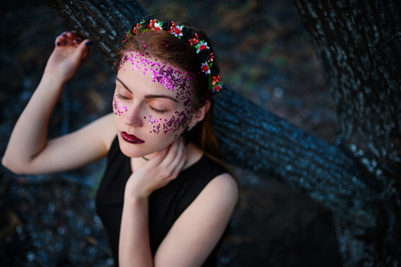 A young beautiful woman with a violet shine on her face stands near a burnt tree.の写真素材