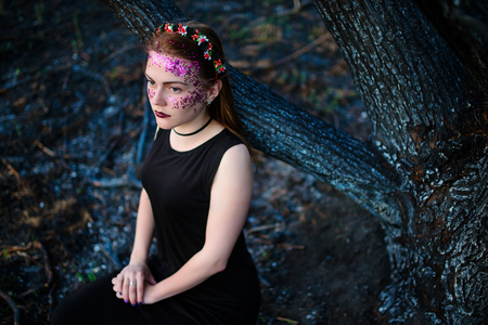A young beautiful woman with a violet shine on her face stands near a burnt tree.の写真素材