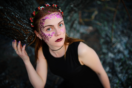 A young beautiful woman with a violet shine on her face stands near a burnt tree.の写真素材