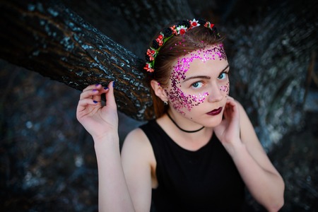 A young beautiful woman with a violet shine on her face stands near a burnt tree.の写真素材