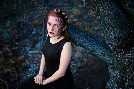 A young beautiful woman with a violet shine on her face stands near a burnt tree.の写真素材