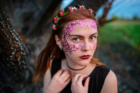 A young beautiful woman with a violet shine on her face stands near a burnt tree.の写真素材