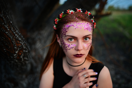 A young beautiful woman with a violet shine on her face stands near a burnt tree.の写真素材