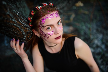 A young beautiful woman with a violet shine on her face stands near a burnt tree.の写真素材