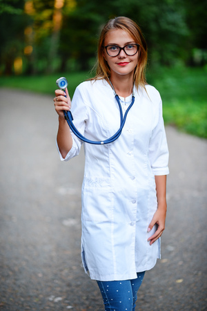 a young girl who is a doctor stands outside, holds the stethoscope in the right hand.の写真素材