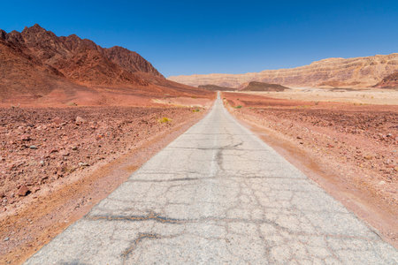 Paved road runs through Arava desert among red mountains in Timna National Park, Israel.
