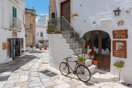 Old bicycle in front of a white wall with stairs and brown wooden doors in the city Ostuni, Apulia, southern Italy.のeditorial素材