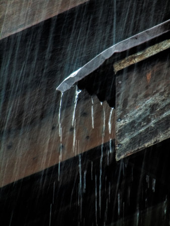 Falling water drops on the roof of a wooden house in the rainの写真素材