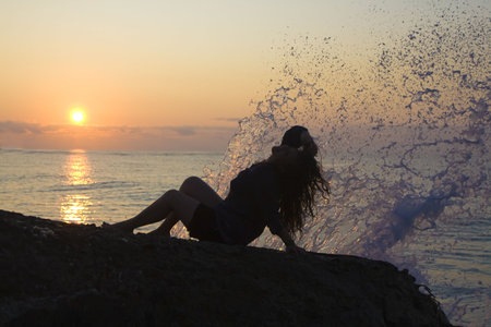 Woman sitting an the beach in sunriseの写真素材