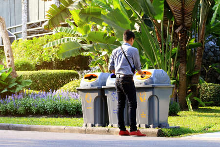Men are dumping plastic bottles waste into trash bin recycle at sideways walk at garden publicの写真素材