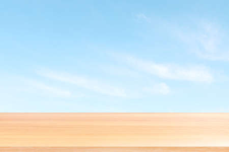 empty wood table floors on blurred blue sky and cloud background, wood table board empty front blur sky blue, wooden plank blank on sky with perspective brown wood table for mock up display productsの写真素材