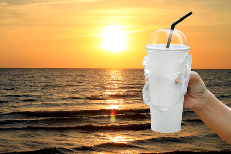 paper cup white and straws in hand over sea beach sunset evening, fast food cup plastic for water...