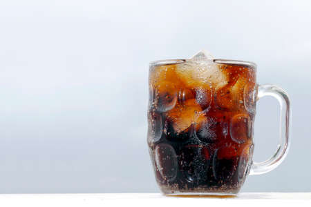 black cola soda in glass with ice cubes for refreshments feel, beverage cola and cubes ice refreshing cool in glass on grey backgroundの写真素材