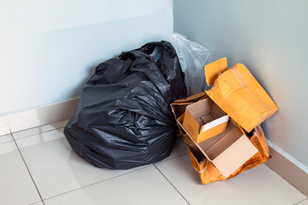 trash, waste, black garbage bag and cardboard boxes piled in the corner of an indoor roomの写真素材