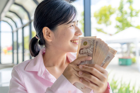 Confident Asian woman holding Thai baht banknotes, Money, Cash, Wealth, symbolizing financial stability, income growth, and personal successの写真素材