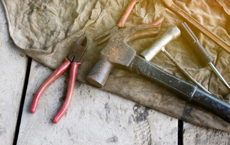 Old hand tools set with hammer and pliers on worn cloth in workshop, Hand tools including a rusty hammer, pliers, and screwdrivers placed on a worn cloth, craftsmanship and repair work, Top viewの写真素材