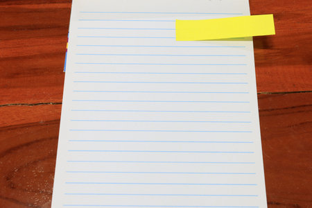 Blank lined paper on wooden desk with yellow sticky note, top view. Minimal flat lay with copy space...