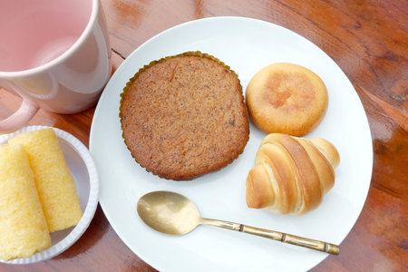Assorted baked goods on a white plate including cake, Bakery set, Round Bun, and mini croissant with...