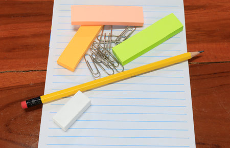 Flat lay of stationery on lined notebook over wooden desk. Pencil, eraser, paper clips, and pastel...