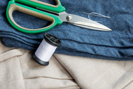 Sewing tools including scissors, blue fabric, and white thread spool, perfect for tailoring,...