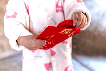 Cute baby holding a red ang pao envelope with gold details, symbolizing luck, blessings, and...