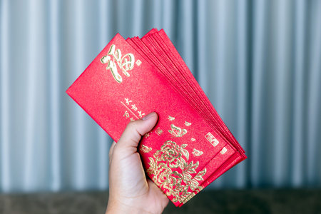 Hand holding red envelopes with golden (Fu) symbol, representing luck, prosperity, and blessings for Lunar New Year or Chinese New Year celebrationの写真素材