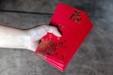 Hand holding red envelopes with golden (Fu) symbol, representing luck, prosperity, and blessings for Lunar New Year or Chinese New Year celebrationの写真素材