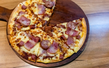 Bacon and sausage pizza with melted cheese served on a wooden tray. Delicious fast food meal from a pizza restaurant with crispy crust and savory toppingsの写真素材