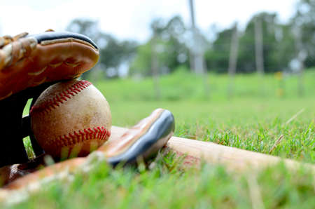 Baseball glove holds ball with bat laying in outfield grass for game.の写真素材