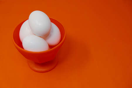 Vibrant orange background and bowl hold fresh white chicken eggs for cooking ingredient.  Copy space for food concept.の写真素材