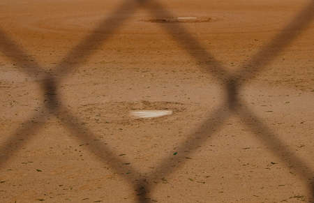 Dirt of baseball field shows game diamond with pitcher's mound through dugout fence.の写真素材