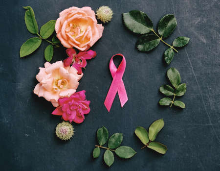Pink breast cancer awareness ribbon with roses and greenery arrangement in circle as feminine flat lay on grunge texture background.の写真素材