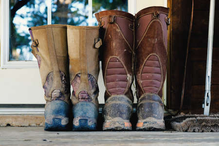 His and hers dirty and mud covered snake hunting boots sitting on doorstep outside.の写真素材