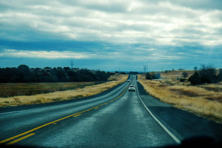 Travel concept with car driving through countryside on road during dreary day.