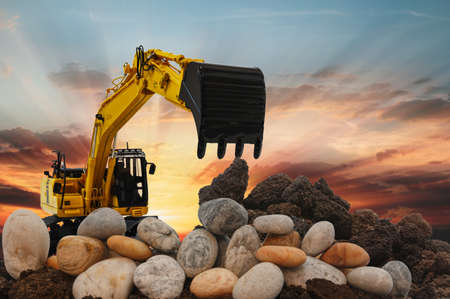 Excavators are digging the soil and stone in the construction site on the sunset backgroundの写真素材