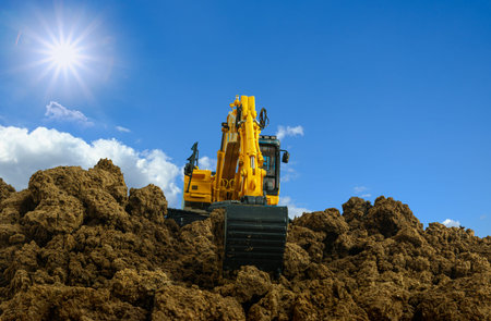 Yellow excavators are digging the soil in the construction site with the sky and sunbeam backgroundの写真素材