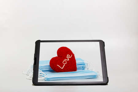 Red heart  shape and  medical  masks in tablet with white background.  Concept of  love and healthcareの写真素材
