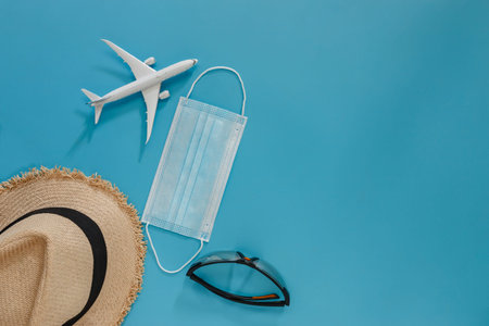Summer holiday blue background with medical mask ,straw hat,  sunglasses,Concept of travel by plane...